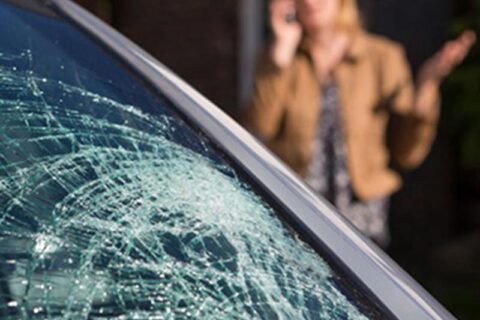 Broken Windshield of a car and a woman talking on the phone in the background